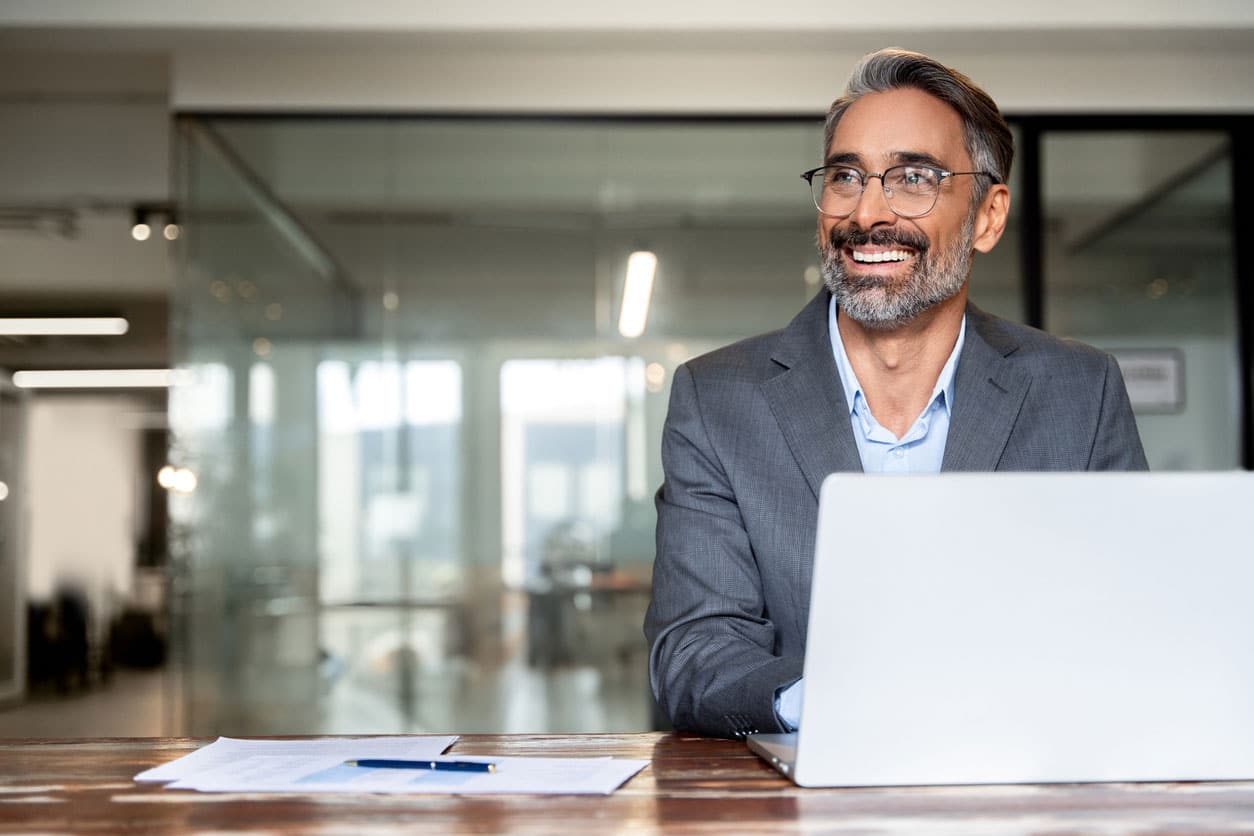 a man sitting at a table with a laptop and smiling at the camera